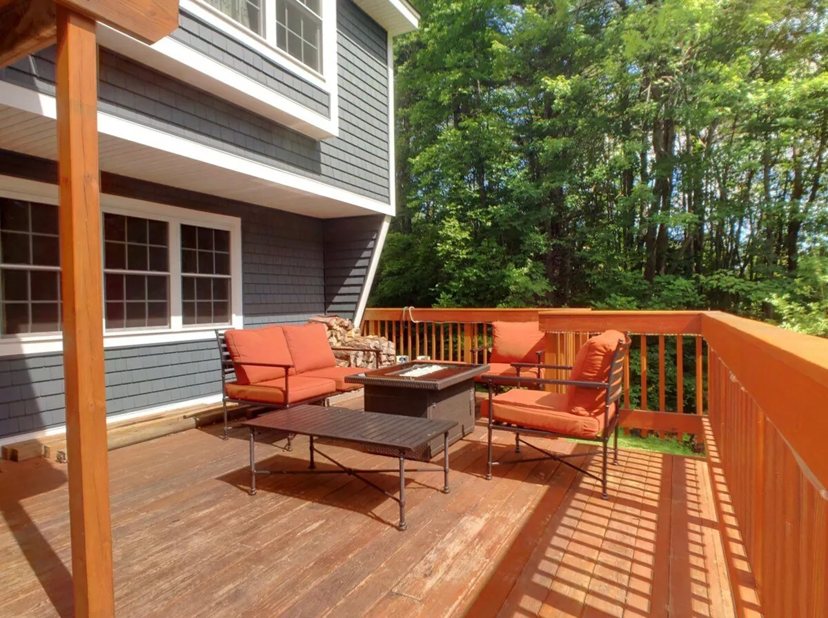 An inviting outdoor seating area sits atop a wooden deck, surrounded by lush greenery. Comfortable chairs and a table create a perfect spot for relaxing or socializing after a day on the slopes. The space is styled for gatherings, with plenty of room to unwind or celebrate together in the fresh mountain air.