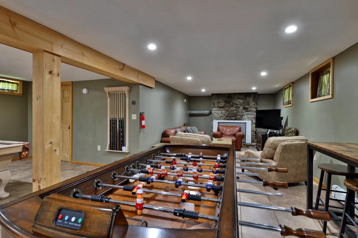 A cozy and playful interior showcasing a foosball table next to a stone fireplace, with a comfortable seating area inviting groups to relax or watch TV. The room’s setup encourages friendly competition and relaxation, capturing the essence of game nights as described in the section.