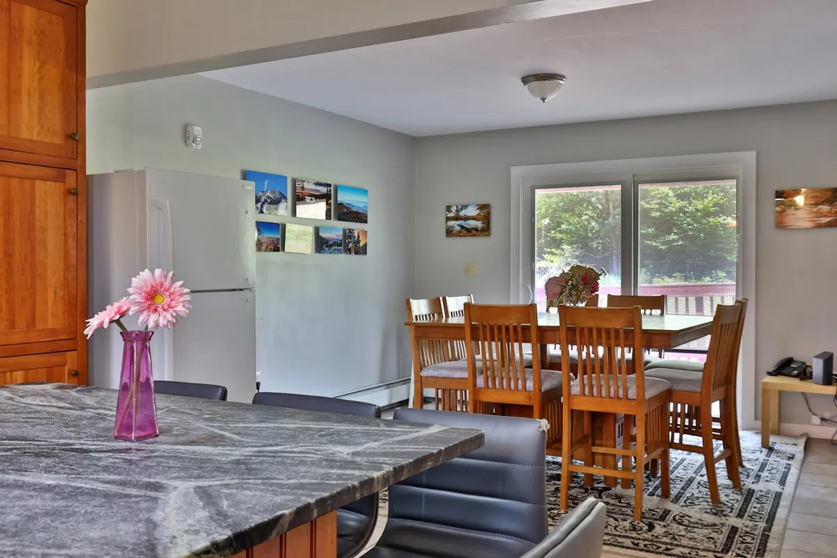 An open-concept kitchen and dining space featuring a kitchen island with a marble countertop, wooden cabinetry, and a dining table with wooden chairs. A vase of flowers adds a touch of warmth and homeliness. The setup is ideal for meal prep, casual breakfasts, and group gatherings.