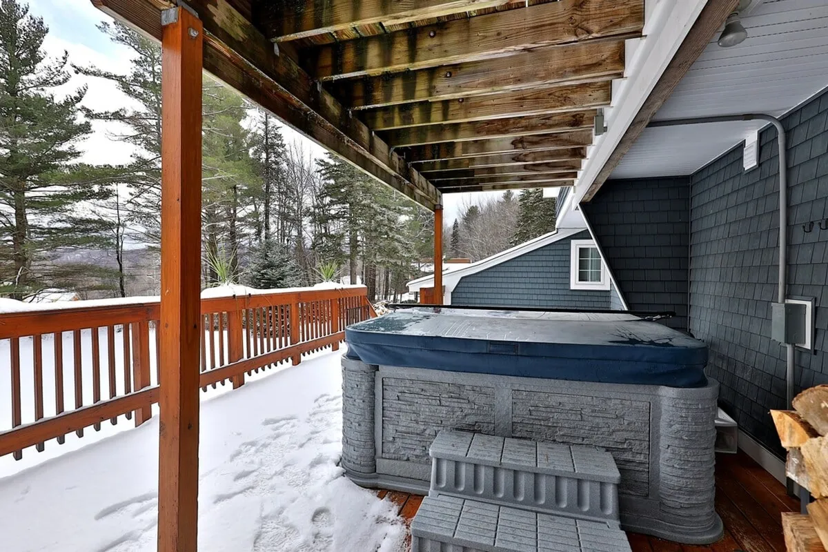 This image captures the outdoor hot tub on a wooden deck, surrounded by snow-covered ground and tall trees, creating a quintessential winter retreat vibe. The steam rising from the tub contrasts with the wintry landscape, evoking relaxation after a day on the slopes.