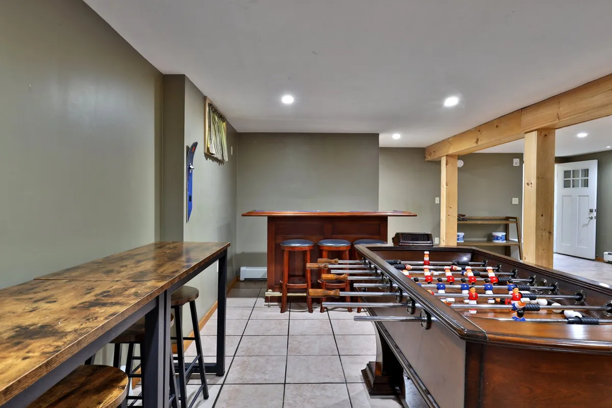 A bright and energetic corner featuring a foosball table and a bar counter with stools, accented by decorative wall art. The setup signals a casual and sociable gathering spot ideal for drinks, games, and making memories with friends or family.