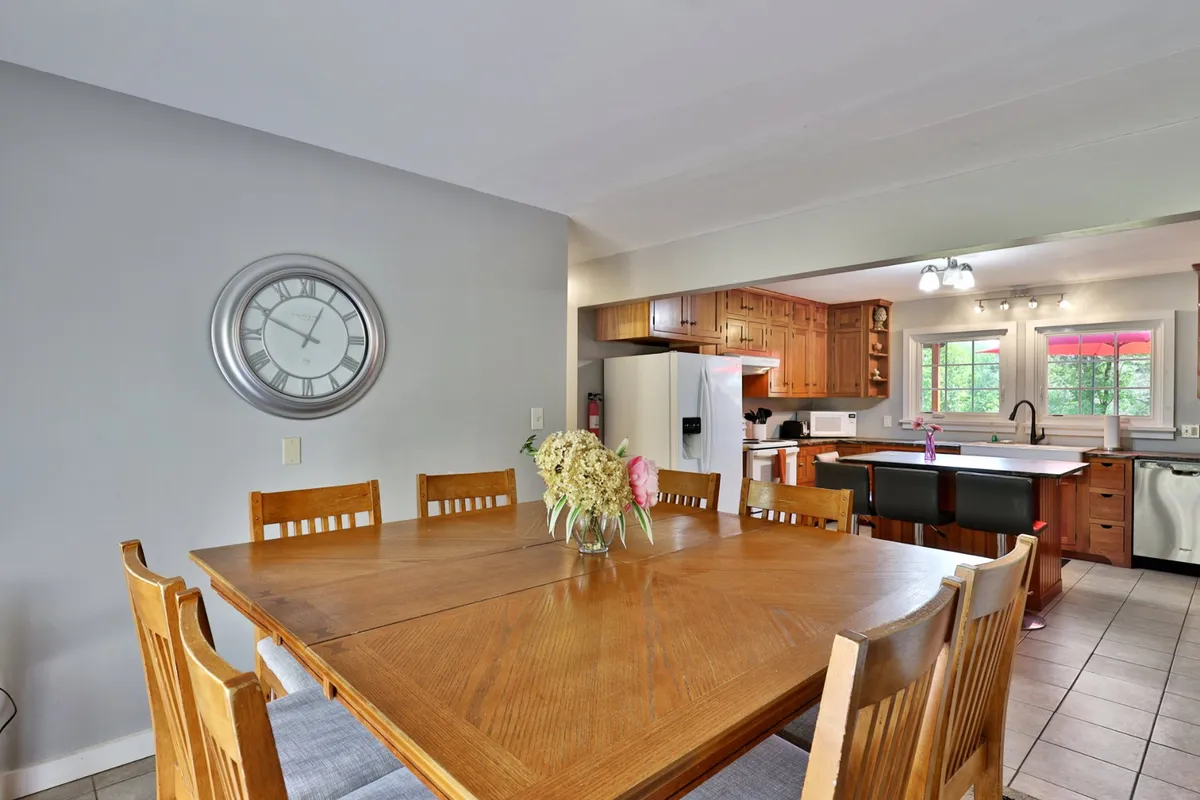 A wide view of the spacious dining area with a large wooden table dressed with a vase of flowers. The layout offers a peek into the adjoining kitchen area, reflecting both the flow and openness of the space. The ambiance is inviting and perfect for family meals and celebrations.