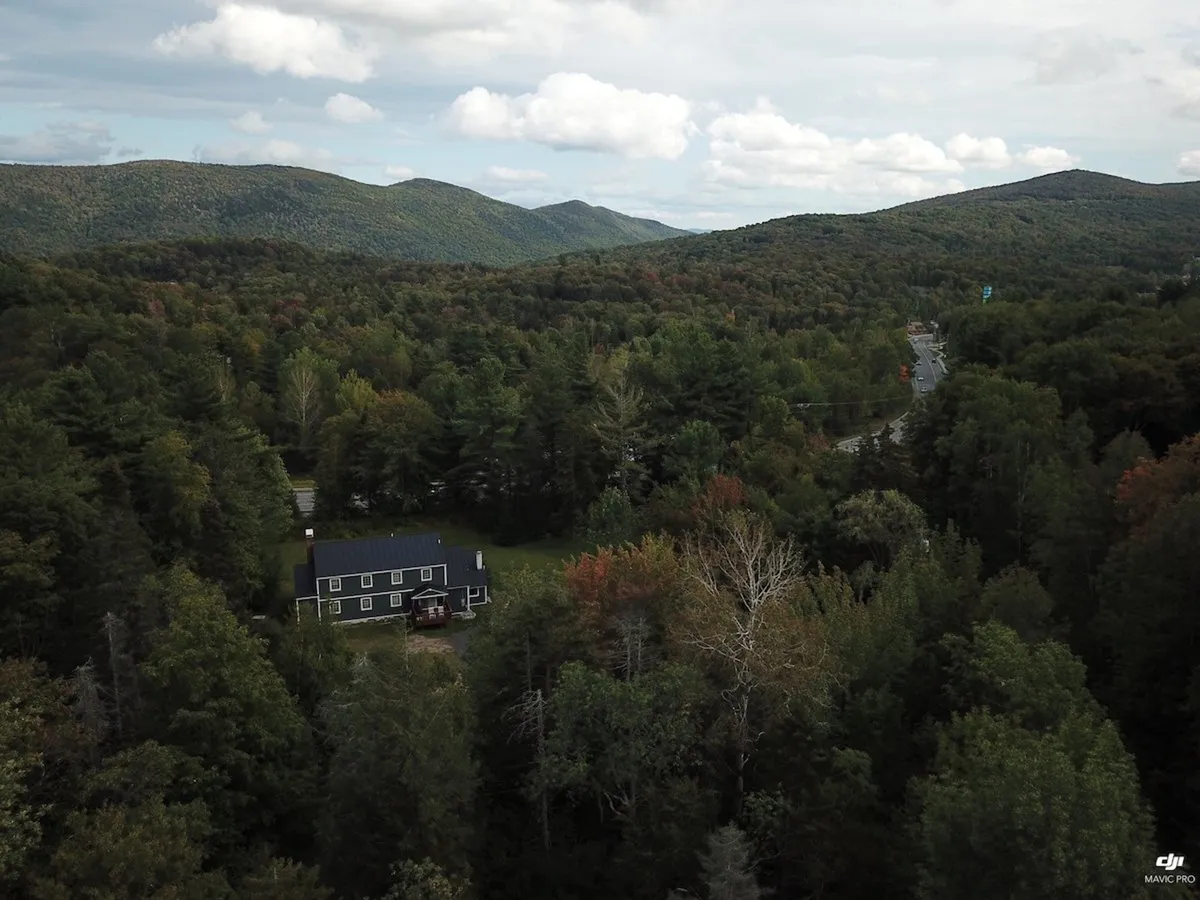 This exterior shot showcases the house nestled among trees, with distant mountains visible in the background. The setting conveys proximity to nature and the mountainous landscape that makes Killington famous for skiing.