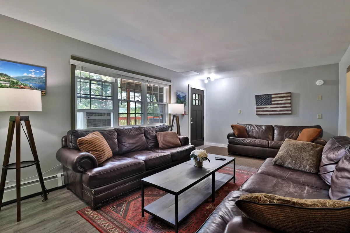 This interior shot presents a cozy living room with leather sofas, a coffee table, decorative rug, and warm lighting. The inviting space is designed for relaxation, perfect for snuggling up indoors with your pet after an adventurous day outside.