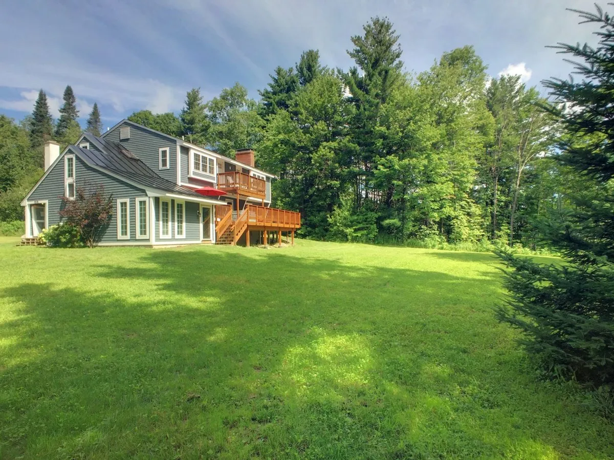 This exterior image showcases the house with its deck, a green lawn, and mature trees in the background. The inviting outdoor space is open and well-maintained, giving a clear sense of where guests and their pets could enjoy the outdoors together, whether for play or relaxation.