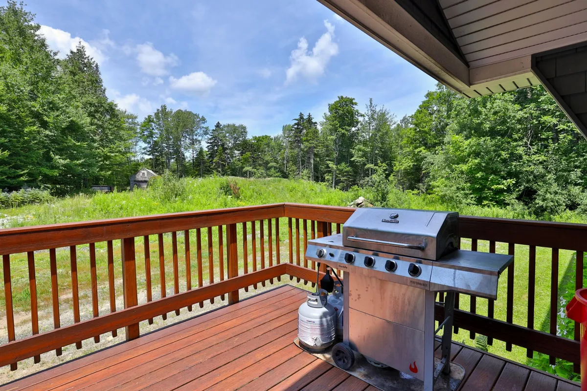 A cheerful exterior deck features a grill, ample seating, and expansive views of greenery and the sky. The setup is ideal for barbecues, evening gatherings, or morning coffee with a group. The environment feels lively and social, making it perfect for entertaining.