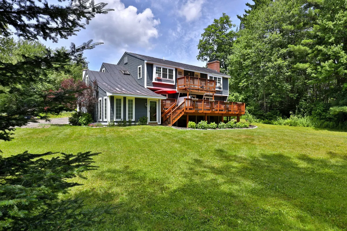 A wide exterior shot highlighting the home's spacious deck, lush green lawn, and the inviting architecture. The scene is set for outdoor dining, family gatherings, or relaxing with friends, with hints of sunset ambiance and views of the garden beyond.
