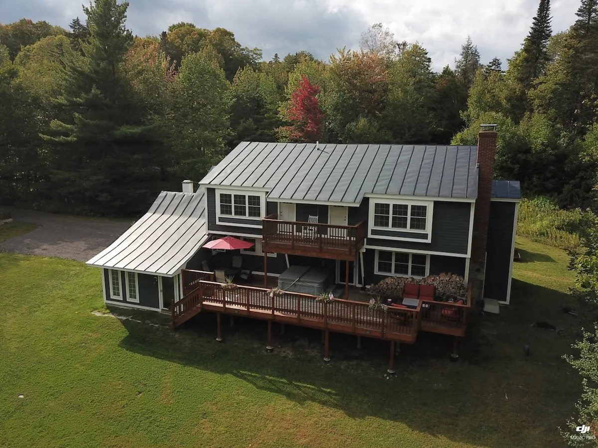 The image captures a modern, spacious wooden deck with comfortable seating, surrounded by colorful autumn foliage and trees. The setting suggests a seamless transition from indoor comforts to outdoor adventure, with ample space for gathering.