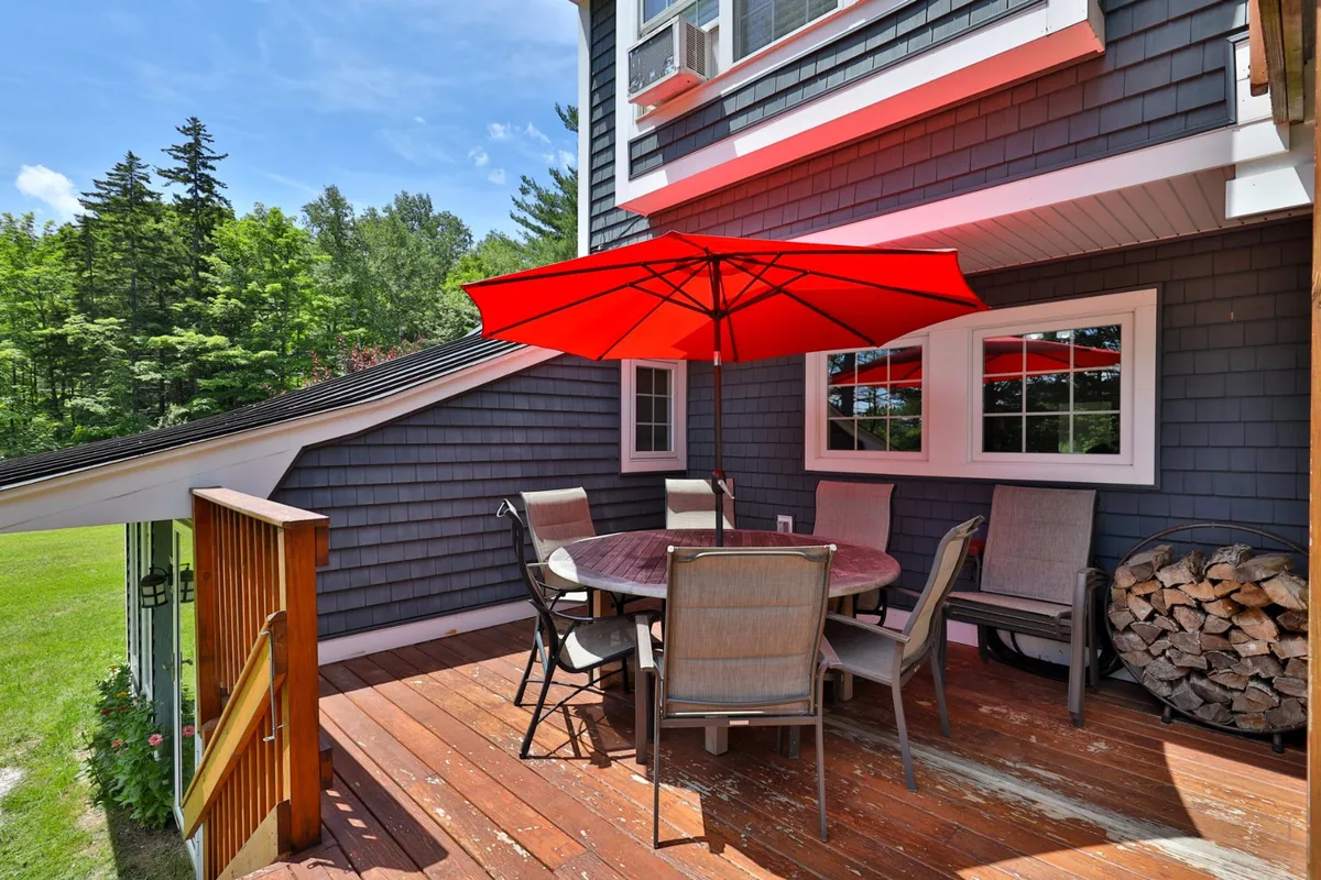 This scene features a cheerful outdoor dining area with a red umbrella, wooden table, and a stack of firewood. The casual seating and natural setting create a vibrant, relaxed mood ideal for socializing or winding down after a day of adventure.