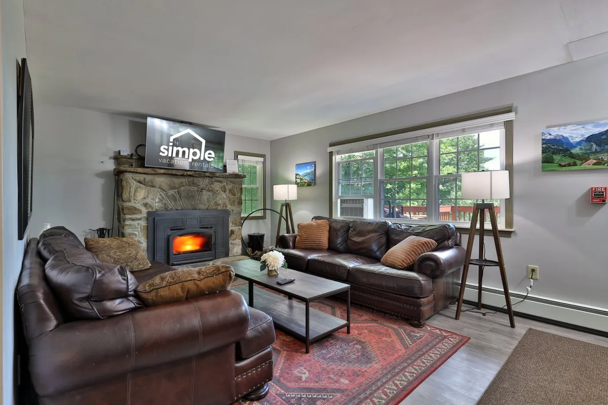 The image showcases a warm and inviting living room with a beautiful stone fireplace as the centerpiece, surrounded by plush, comfortable sofas and a decorative rug. A television is placed for entertainment, creating a perfect space for relaxing, watching movies, or gathering with friends and family after a day on the slopes.