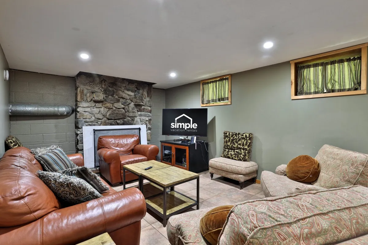 A cozy living area featuring a stone fireplace, leather sofas, and a textured armchair arranged around a wooden coffee table. The setup invites guests to socialize, play games, or relax with a movie, emphasizing comfort and togetherness.