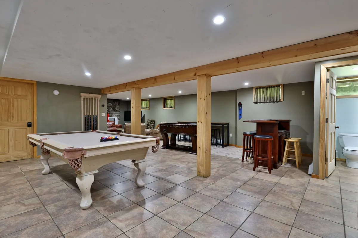 This image features the heart of the game and entertainment zone: a spacious room with a pool table at the center, a bar area for drinks and snacks, and a game table for additional activities. The room’s layout is open and inviting, designed for socializing and leisure. The lighting, decor, and setup emphasize a relaxed, fun atmosphere perfect for gatherings and friendly competition.